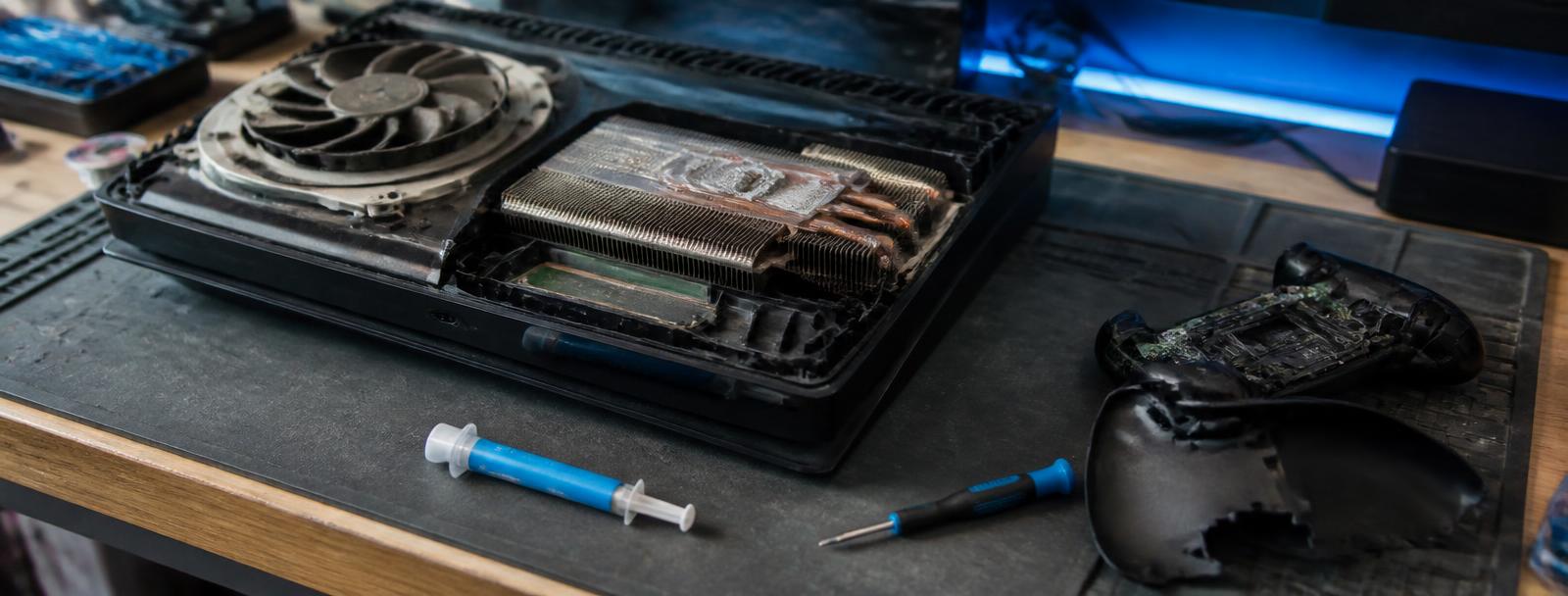 Games console opened on a repair bench with cooling fan and heatsink exposed
