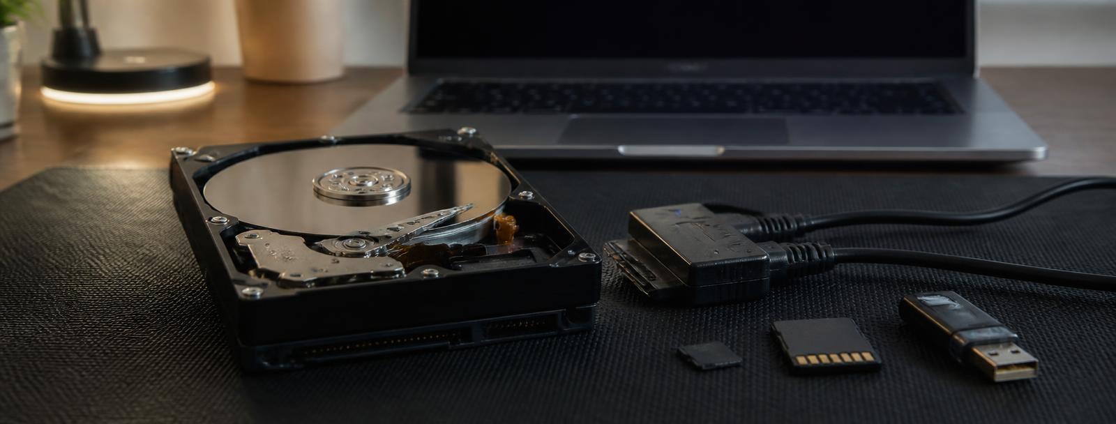 Data recovery specialist inspecting an opened hard drive next to a laptop running recovery software