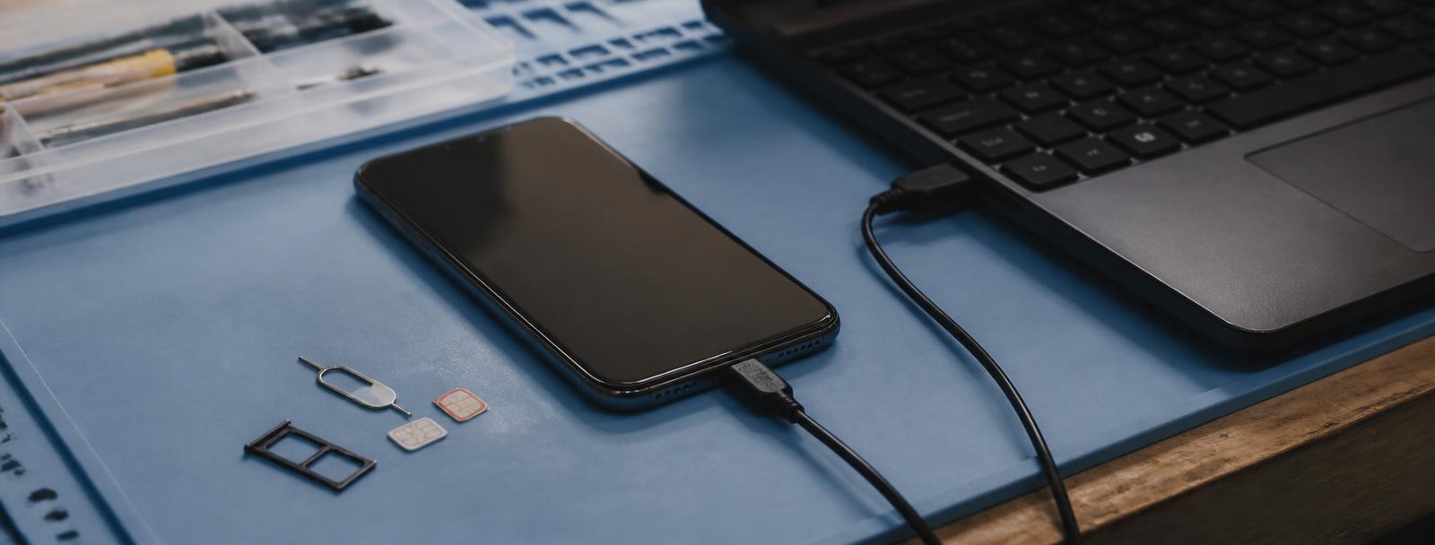 Technician unlocking a smartphone connected to a laptop running unlocking software